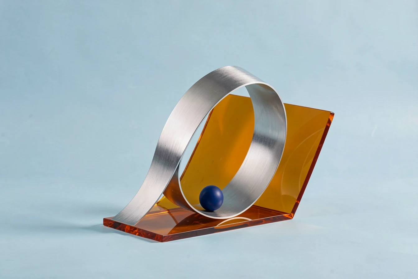 A sculptural ribbon of brushed chrome folded through translucent amber and pale blue material.