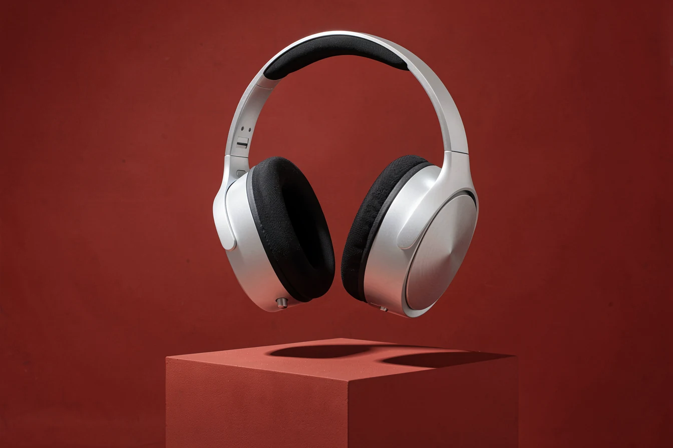 Unbranded sculptural silver over-ear headphones suspended above a red sculptural platform.